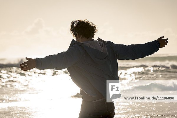 Glücklicher junger Mann mit ausgestrecktem Arm am Strand