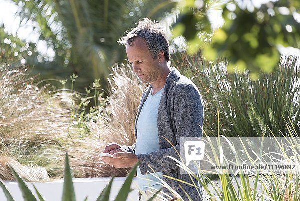 Mann mit dem Handy im Garten