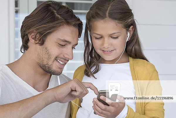 Happy father with his little daughter listening to music on mobile phone with earbuds