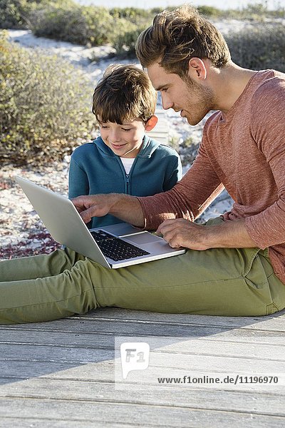 Father and son using a laptop on boardwalk