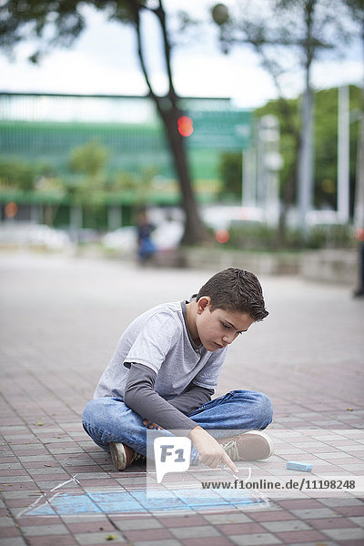 Hispanic boy drawing laptop with chalk on sidewalk