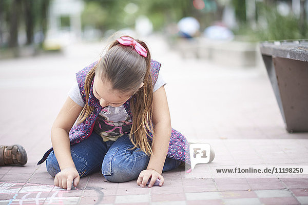 Hispanic girl drawing with chalk on sidewalk