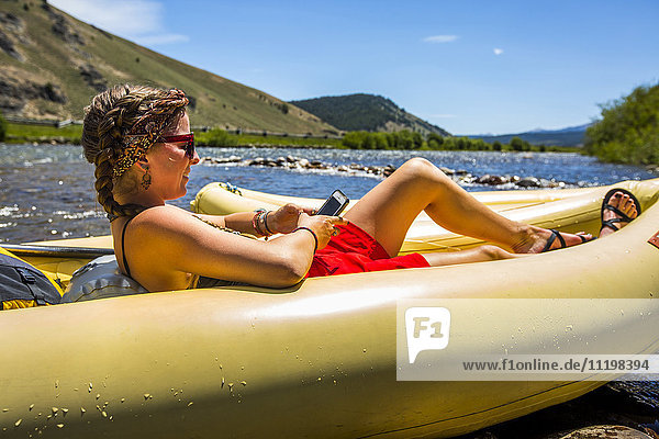 Caucasian woman laying in inflatable raft texting on cell phone