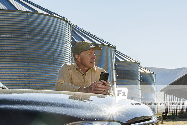 Kaukasischer Landwirt lehnt sich an einen Lastwagen und schreibt eine SMS mit seinem Handy
