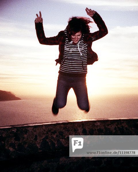 Junge Frau springt bei Sonnenuntergang mit Meer im Hintergrund  3D-Stereo-Effekt