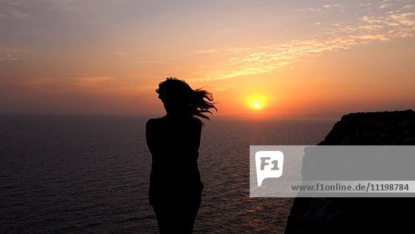 Rückansicht Silhouette einer Frau mit Blick auf das Meer bei Sonnenuntergang