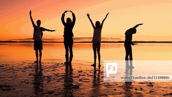 Silhouette von vier Personen  die am Strand bei Sonnenuntergang mit ihren Armen LIEBE buchstabieren