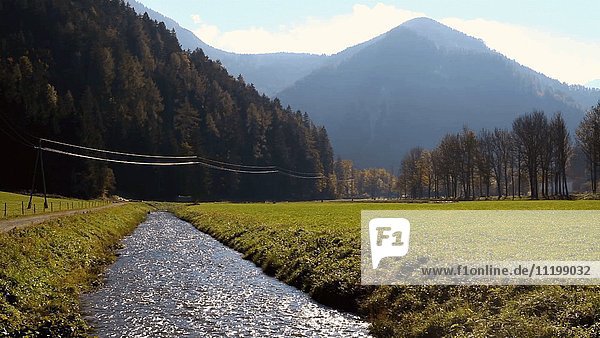 Bach fließt durch grünes Feld mit Bergen im Hintergrund