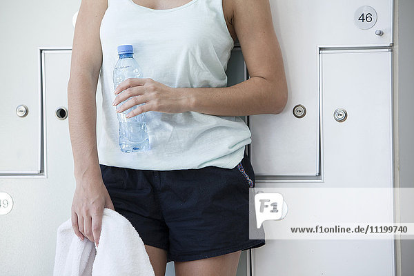 Woman leaning against lockers  with towel and bottled water  cropped