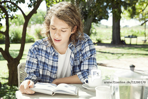 Junger Mann beim Lesen eines Buches bei einer Tasse Kaffee