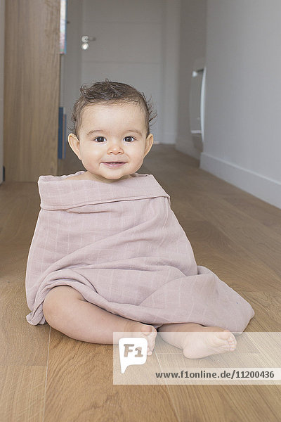 Baby auf dem Boden sitzend  in eine Decke gehüllt  Portrait
