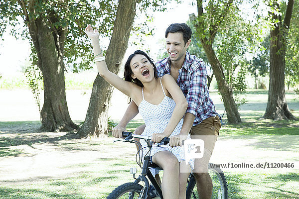 Young couple riding bicycle together with girlfriend seated sidesaddle on crossbar
