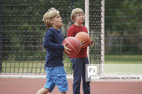 Jungs halten Basketbälle  während sie auf den Platz schauen.