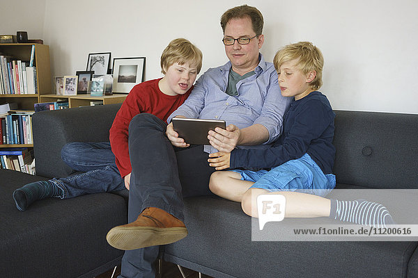 Vater und Söhne sitzen auf dem Sofa und benutzen zu Hause ein digitales Tablett.
