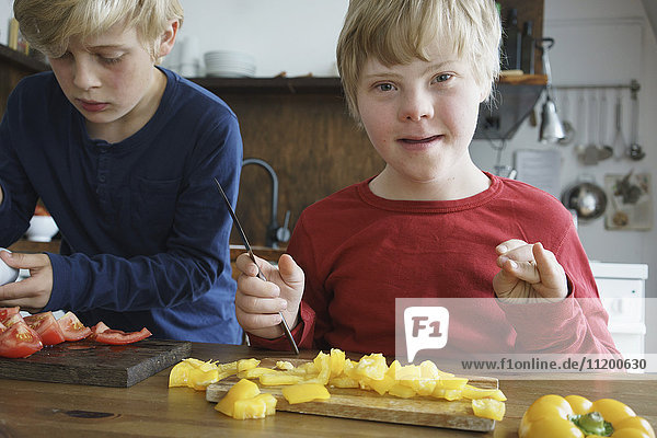 Portrait of disabled boy sitting by brother at table with vegetables in kitchen