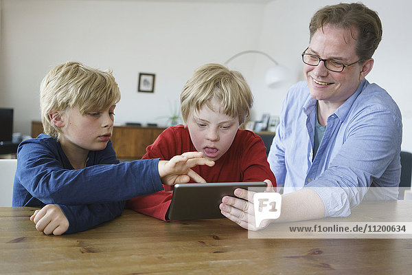 Lächelnder Vater mit Söhnen bei Tisch im Haus mit digitalem Tablett