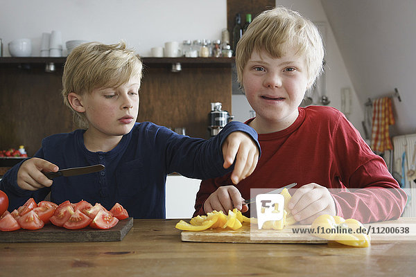 Portrait of disabled boy sitting with brother at table with vegetables in kitchen