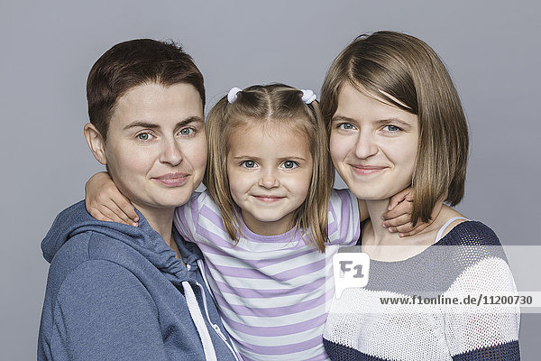 Porträt eines lächelnden Mädchens mit Mutter und Schwester vor grauem Hintergrund