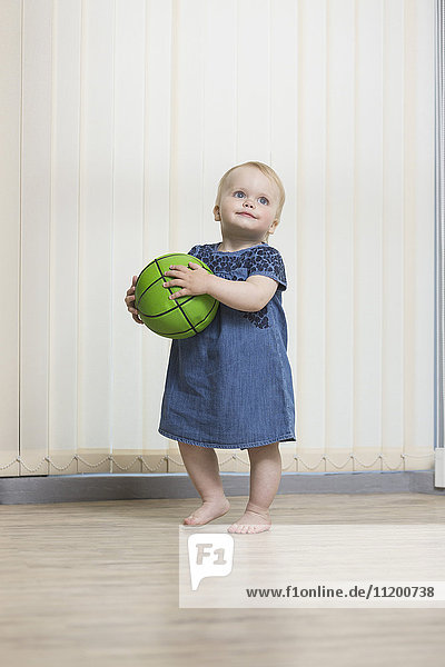 Süßes Mädchen  das mit dem Ball spielt  während es zu Hause gegen Vorhänge steht.