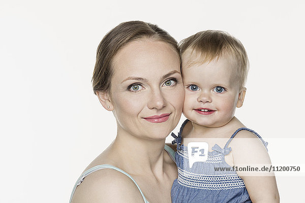 Portrait of smiling mother carrying cute girl against white background