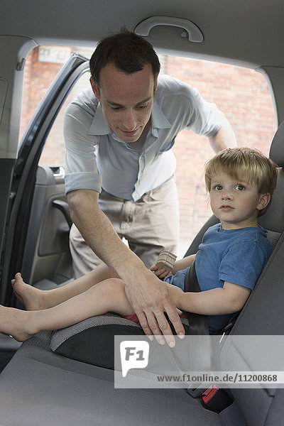 Father fastening seat belt for boy in back seat of car