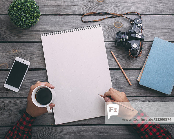 Beschnittenes Bild eines Mannes  der eine Kaffeetasse hält  während er auf Papier schreibt.