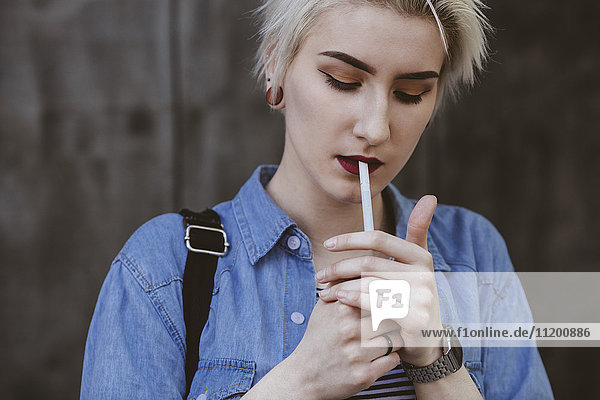 Young fashionable woman smoking cigarette while standing outdoors