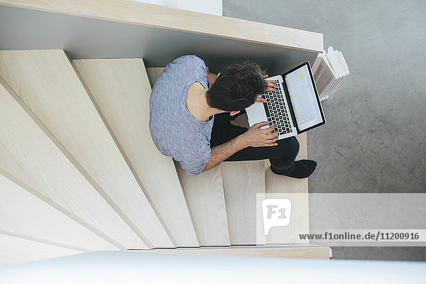 Mann mit Laptop auf einer Treppe sitzend