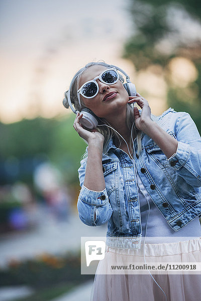 Modische junge Frau mit Sonnenbrille beim Musikhören über Kopfhörer