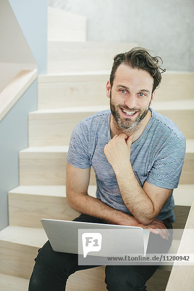 Smiling man with laptop sitting on stairs