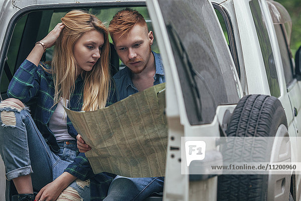 Couple analyzing map while sitting in off-road vehicle at forest