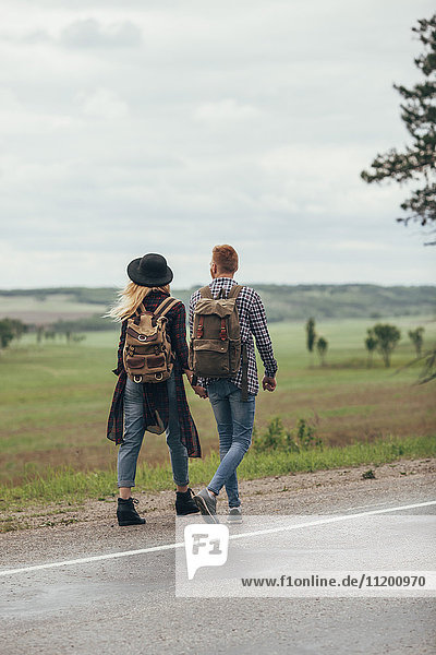 Couple walking on roadside by field against sky