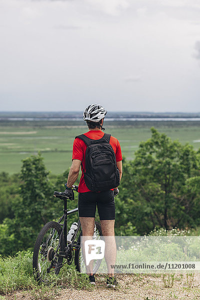 Rear view of man standing with mountain bike on hill