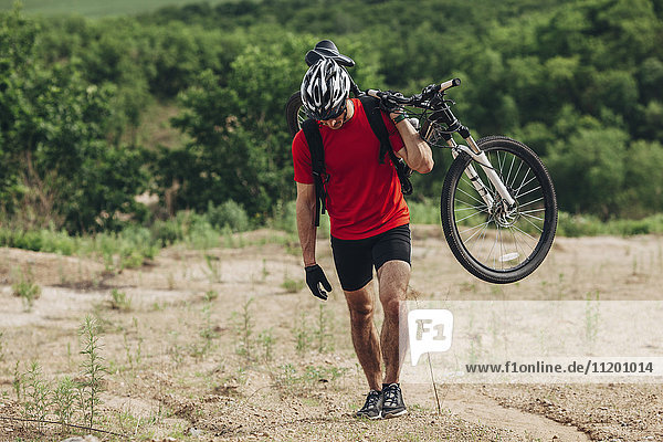 Determined man carrying mountain bike up hill