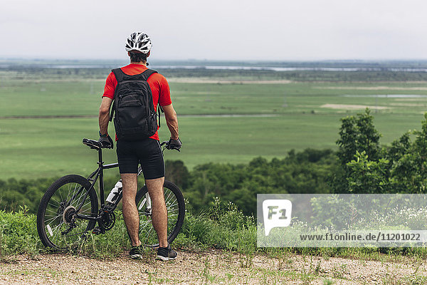 Rear view of man with mountain bike standing on hill