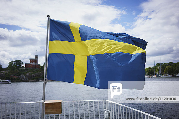 Schwedische Flagge am Geländer mit Wasser gegen bewölkten Himmel