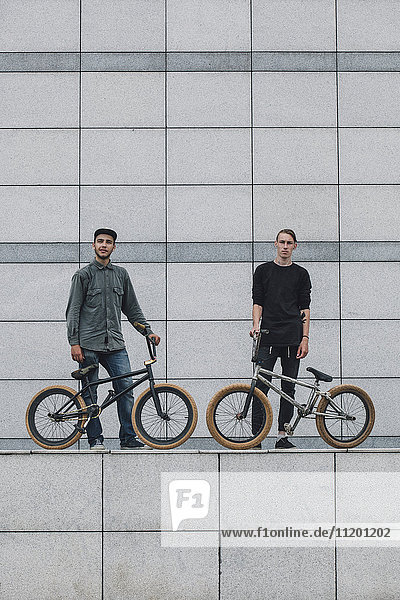 Confident teenagers with bicycles standing against wall at skateboard park