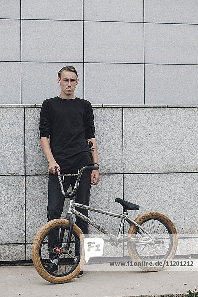 Teenager standing with bicycle against wall