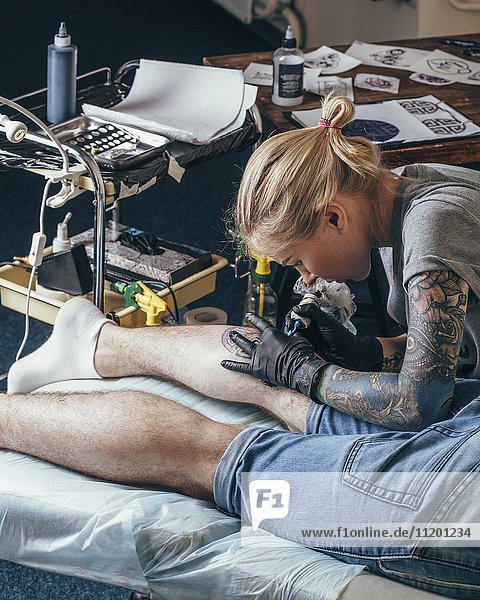 Künstler Tätowierung Design auf dem Bein des Mannes im Studio