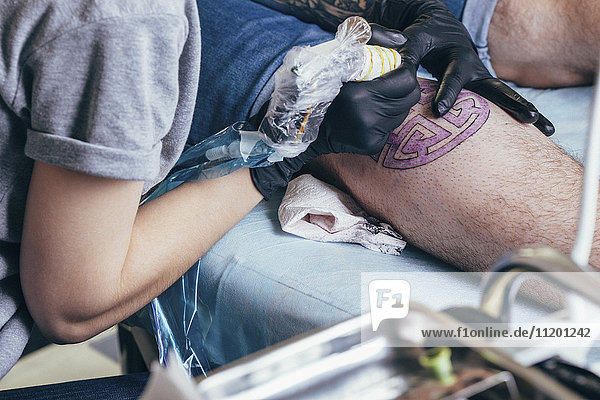 Künstler Tätowierung lila Design auf dem Bein des Mannes im Atelier