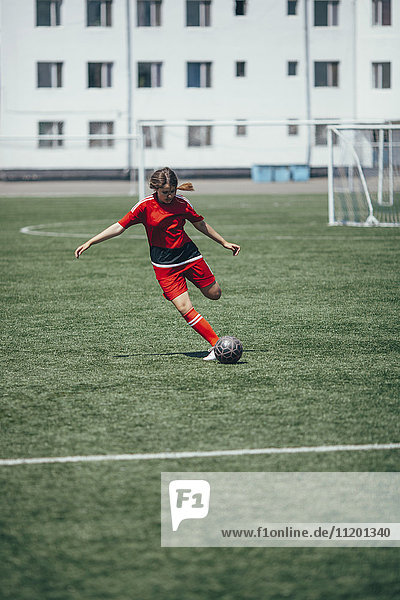 Entschlossener Teenager tritt Ball auf Fußballplatz
