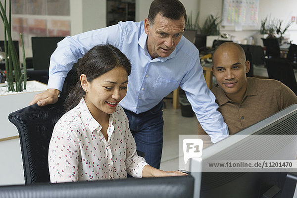 Lächelnde Geschäftsleute  die während der Besprechung im Kreativbüro auf Computer schauen