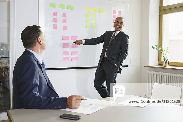 Happy businessman explaining to male colleague in meeting at creative office