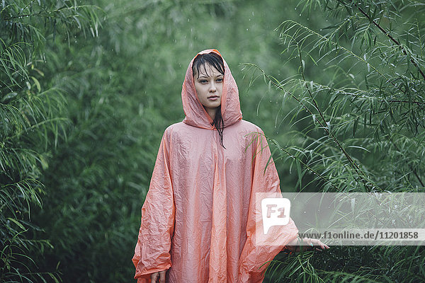 Junge Frau im Regenmantel inmitten von Pflanzen während der Regenzeit
