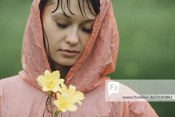 Nahaufnahme der schönen Frau im Regenmantel mit gelben Blumen in der Regenzeit
