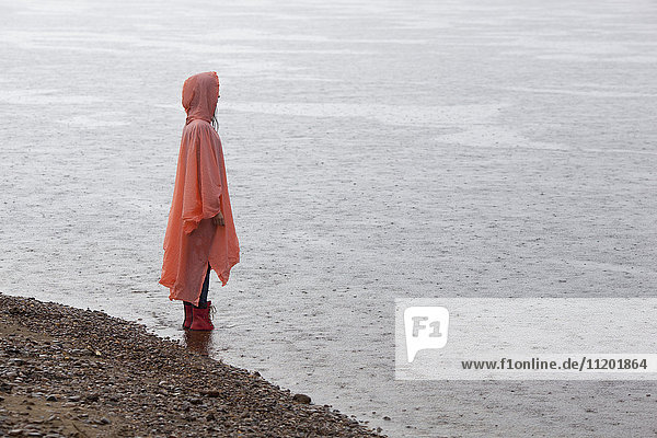 Frau im Regenmantel am Seeufer stehend in der Regenzeit