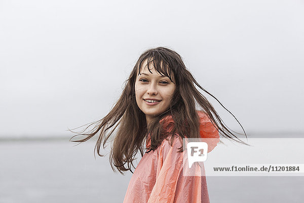Porträt einer fröhlichen Frau im Regenmantel am klaren Himmel