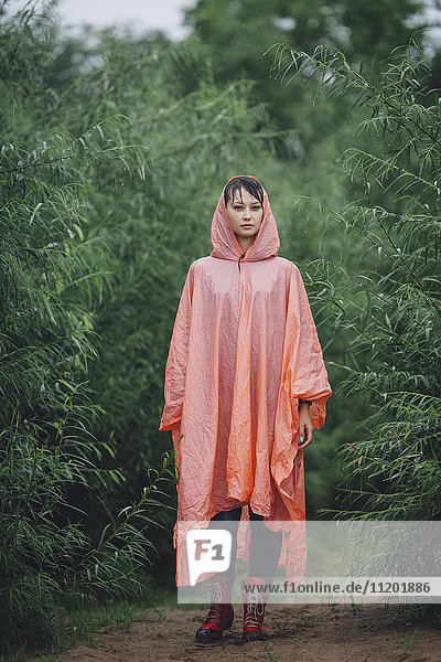Porträt einer Frau im Regenmantel  die während der Regenzeit inmitten von Pflanzen steht.