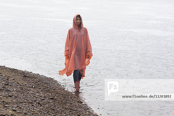 Frau im Regenmantel  die während der Regenzeit am Seeufer spazieren geht.