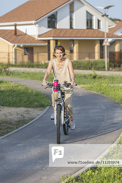 Portrait of woman riding bicycle on road against house